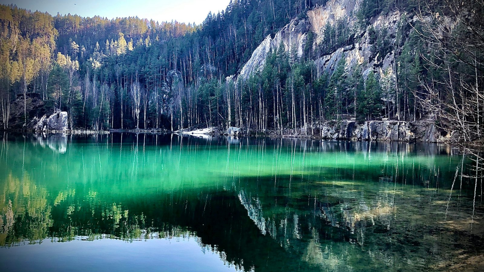 Lago turquesa al pie de una pared rocosa cubierta de bosque
